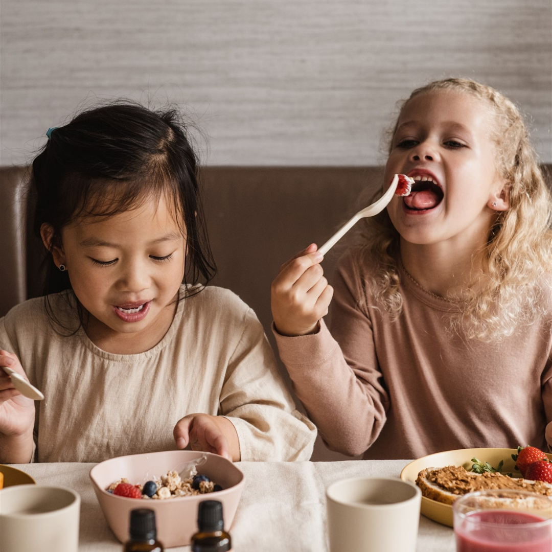 Sfeerfoto van de vitaminedruppels met twee kindjes op de foto die aan een gezond ontbijtje zitten.