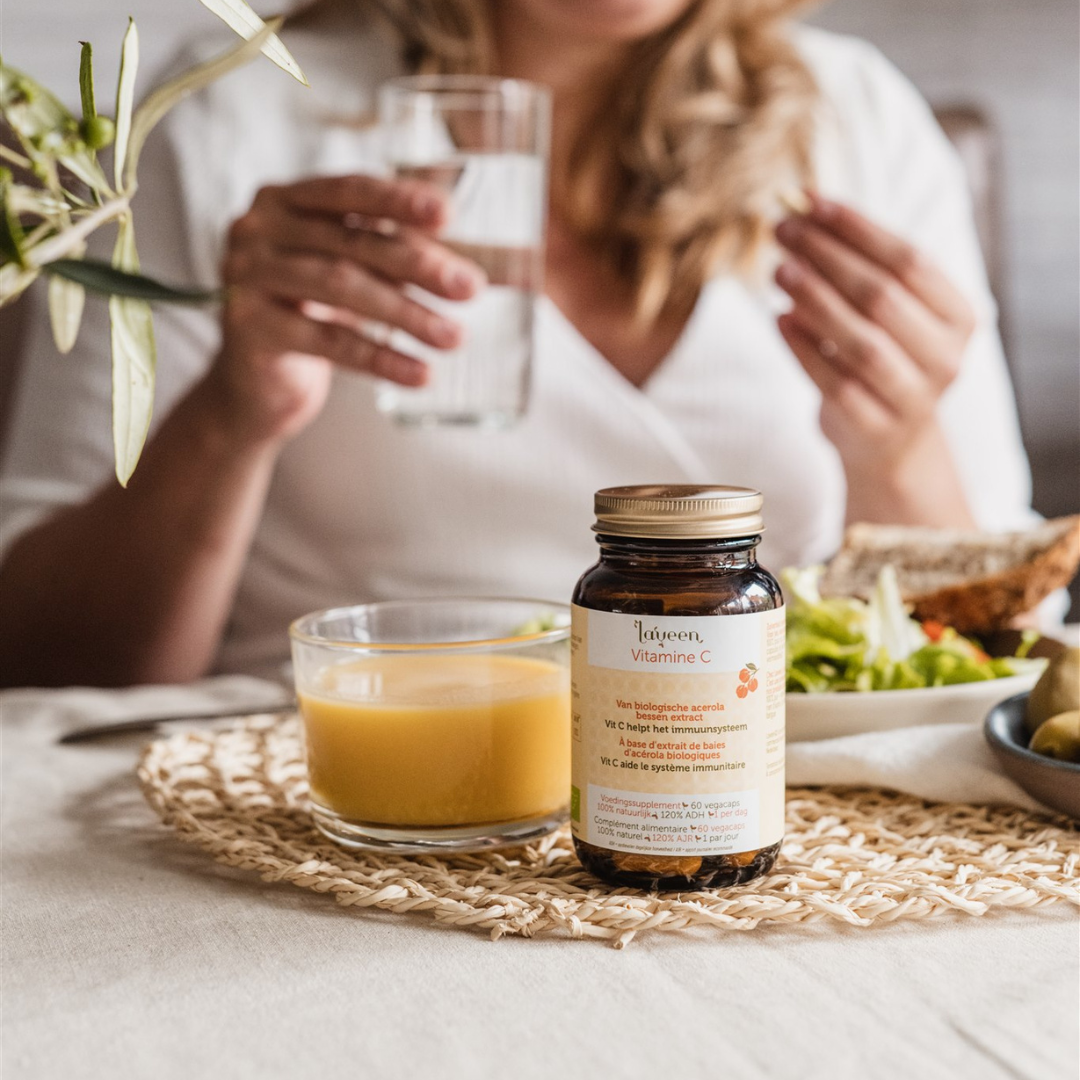 Sfeerfoto van de Bio Vitamine C., een model neemt een capsule met een glas sinaasappelsap.