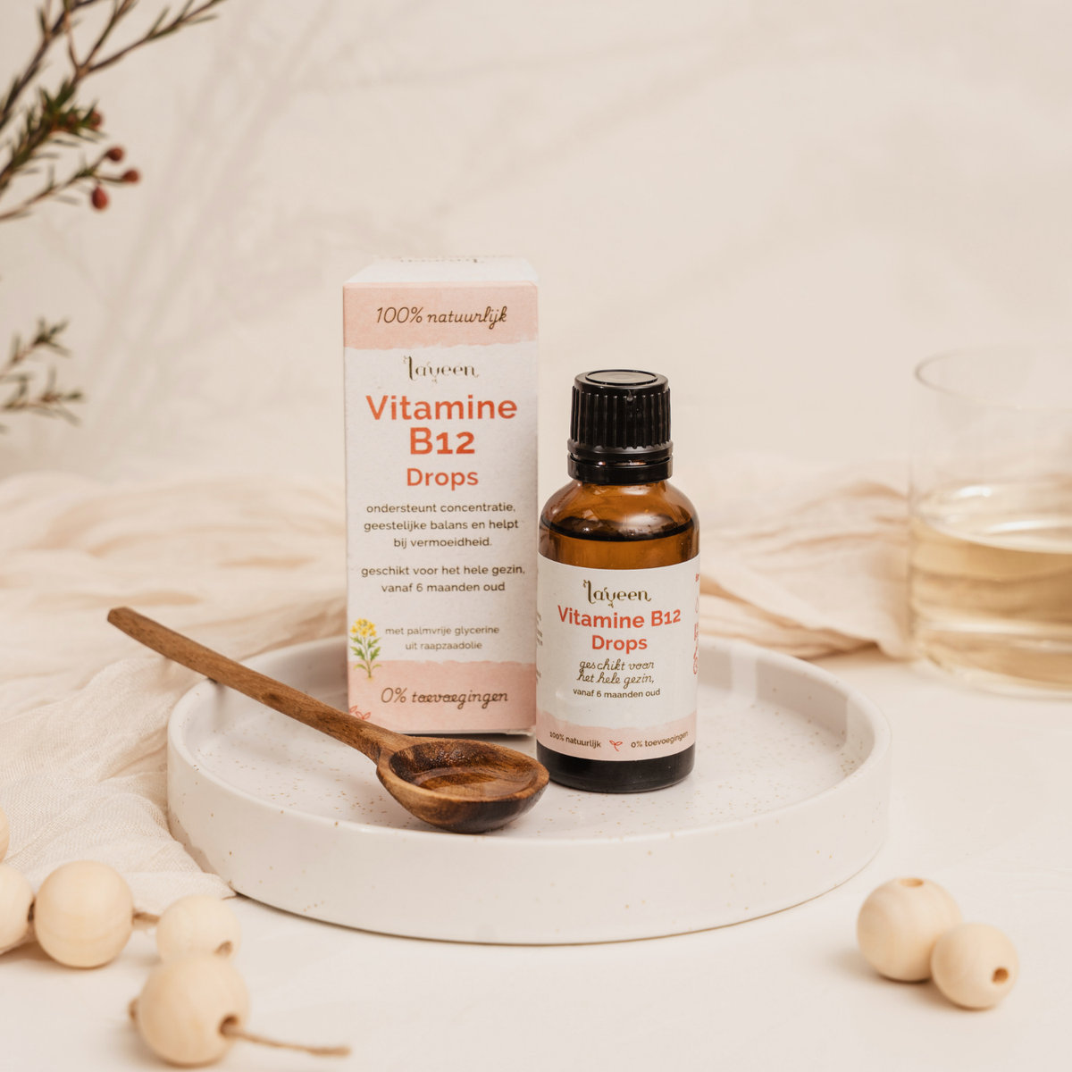 Laveen Vitamine B12 druppels in glazen flesje met verpakking op een schaaltje, naast een houten lepel, geschikt voor het hele gezin vanaf 6 maanden en zonder toevoegingen