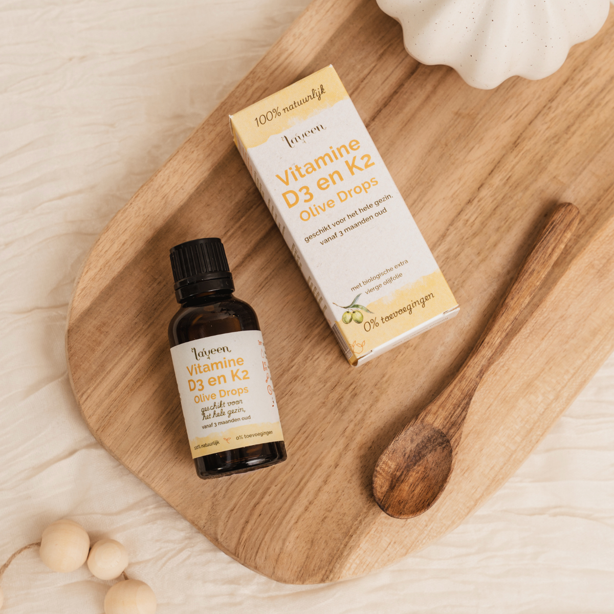Flesje en verpakking van Laveen Vitamine D3 en K2 druppels op een houten plank met lepel. Geschikt voor het hele gezin vanaf 3 maanden, op basis van olijfolie en zonder toevoegingen.